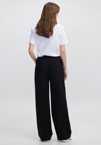 Witte kortebloes met korte mouwen gecombineerd met zwarte wijde broek. De outfit heeft een gladde textuur en een ontspannen pasvorm.