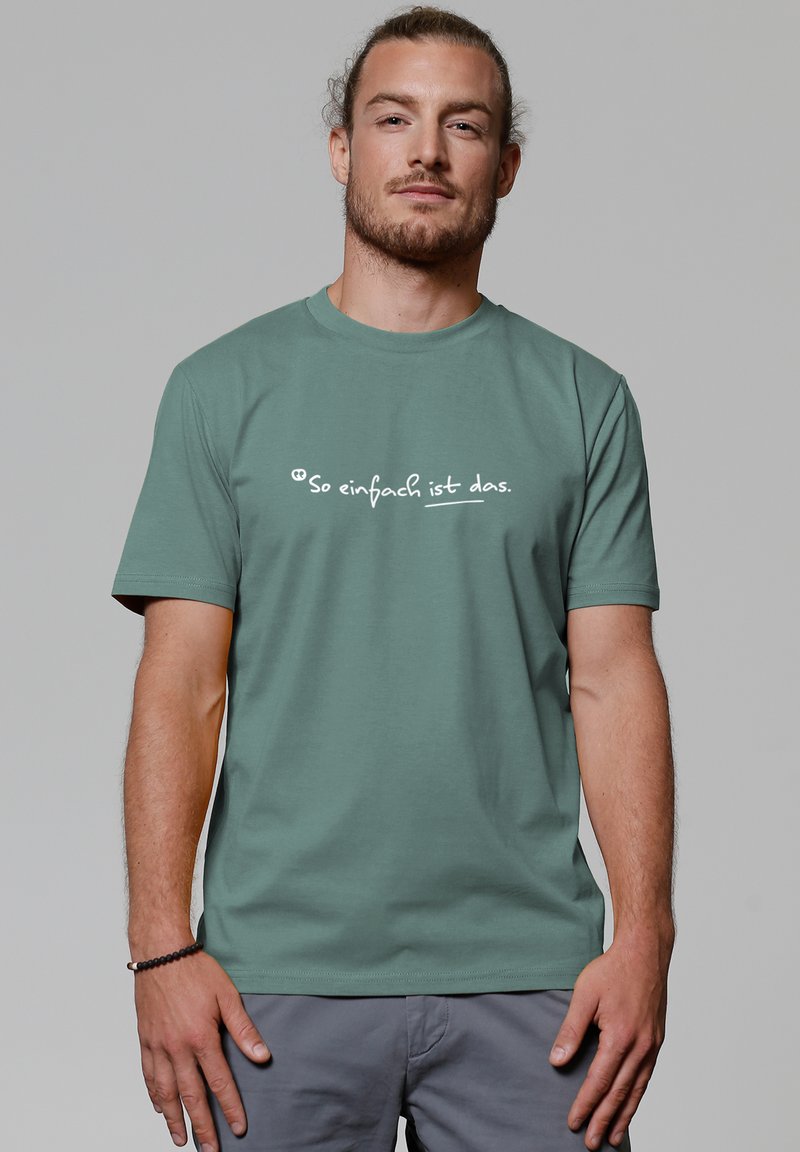 Groene katoen t-shirt met witte tekst die "So einfach ist das" op de borst leest. Korte mouwen en een klassiek rond decolleté ontwerp.