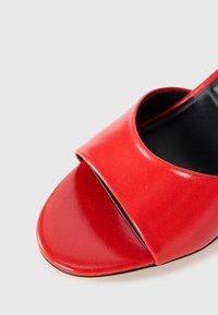 Red leather open-toe shoe with a glossy finish, featuring a wide strap across the instep and a curved silhouette. Black interior.