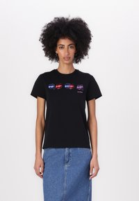 Black cotton t-shirt featuring four stylized fish graphics in red and blue. Short sleeves, crew neck, relaxed fit. Denim skirt completes the look.