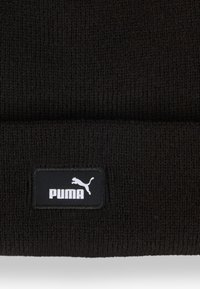 Beanie lavorato a maglia nero con risvolto. Presenta un'etichetta con il logo bianco "PUMA" su sfondo nero. Tessuto morbido e texturizzato.