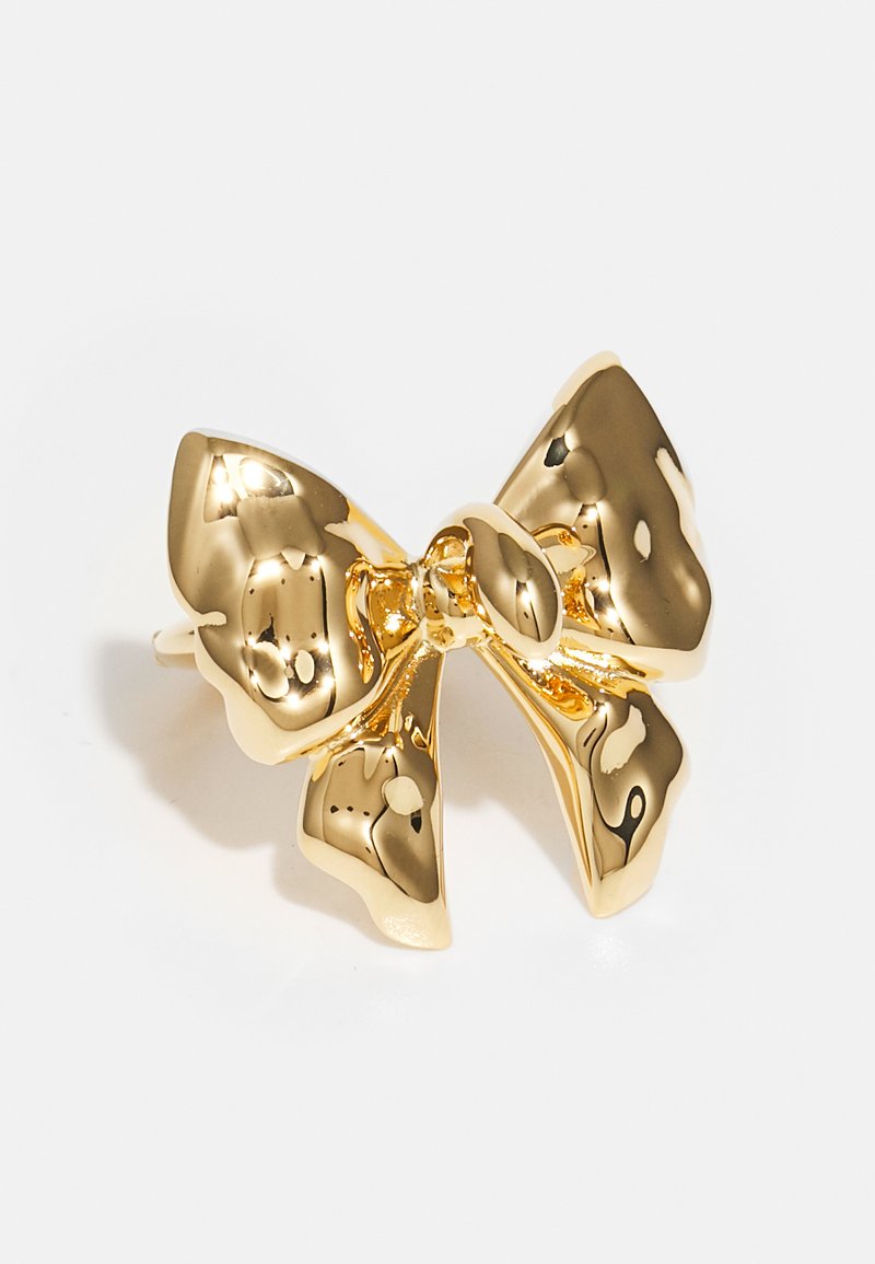 Clipe de cabelo em forma de arco dourado com uma superfície brilhante e reflexiva. Apresenta bordas suaves e curvadas, além de um detalhe de nó central para um fecho seguro.