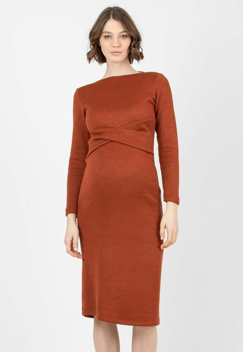 Robe longue à manches longues de couleur rouille avec une silhouette ajustée, présentant un détail torsadé à la taille et un ourlet au genou. Texture lisse.