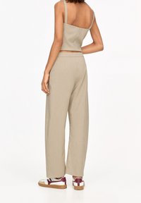 Crop top en ribbed beige avec des bretelles fines associé à un pantalon beige ample. Les chaussures présentent des accents blancs, bordeaux et marron.