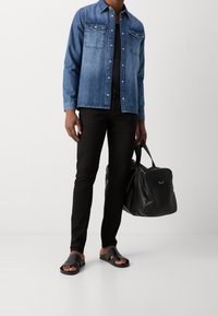 Koszula dżinsowa, czarne obcisłe dżinsy, czarna skórzana torba oraz czarne klapki na płaskim obcasie. Elementy wyróżniające to dwie kieszenie na piersi i zapięcie na guziki.