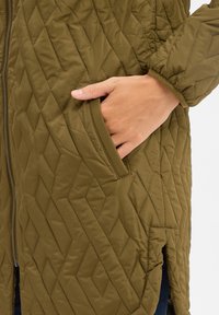 Giacca trapuntata verde oliva con motivo a rombi, chiusura con zip, tasche laterali e orlo leggermente svasato. Tessuto morbido e traspirante.