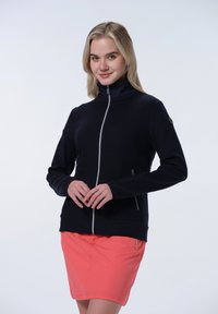 Marinblå fleecejacka med hög krage, med långa ärmar, sidofickor och en kontrasterande dragkedja. Bärs med en rosa kjol.