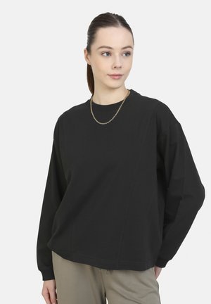Black long-sleeve sweatshirt with a round neckline, loose fit, and side seams. Paired with light-colored pants and a minimalist chain necklace.