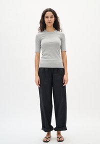 Top gri cu dungi, cu mânecă scurtă, asociat cu pantaloni negri cu croială largă. Design simplu, textură netedă și fără modele sau detalii vizibile.