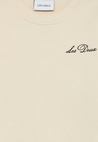 Felpa crema con colletto a coste e un piccolo logo nero "Les Deux" ricamato sul davanti. Materiale morbido con una texture liscia.