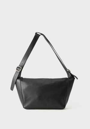 Bolso de hombro negro de cuero con correa ajustable y hebilla plateada, de forma trapezoidal y cierre superior con cremallera.