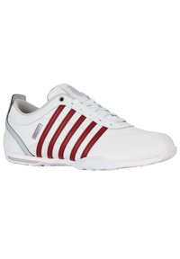 Weiße Sneakers mit roten und grauen Akzenten, ausgestattet mit einem glatten Synthetik-Obermaterial, sechs Ösen und einer strukturierten Gummisohle.