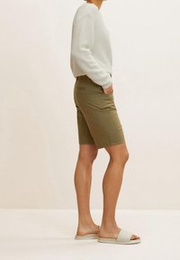Lichtgrijze gestreepte trui, olijfgroene shorts en beigekleurige gewatteerde slidesandalen. Focus op een relaxte pasvorm en comfortabele materialen.