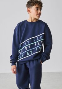 Marineblauer Pullover mit weißen und türkisfarbenen horizontalen Streifen und dem Schriftzug "KEEPER BY TED"; lockere Passform; kombiniert mit passenden Hosen.
