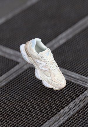Neutral-toned sneaker with textile and mesh upper, padded collar, lace-up front, and rubber sole. Features light blue accents and ‘N’ logo.