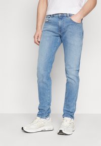 Lys blå denimjeans med slim fit, som har fem lommer og subtile slitasjer på lårene. Sammen med hvite joggesko.
