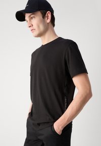 Čierne bavlnené tričko s okrúhlym výstrihom a krátkymi rukávmi. Na bočnom šve je vyznačené logo "Calvin Klein Jeans". Skombinované s čiernymi nohavicami.