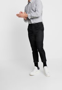 Camicia button-up a righe in blu chiaro e bianco, abbinata a pantaloni neri slim-fit e sneakers bianche con dettagli blu navy.