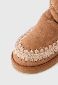 Pruuni seemsne saabas keerulise beeži tikandiga ülemise serva ümber, ümar varvas ja tekstureeritud kummipõhi.