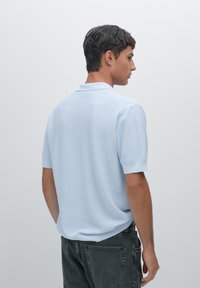 Polo shirt azzurro chiaro con una trama tessuta, maniche corte e colletto classico. Indossato con jeans grigio scuro, visto da dietro.