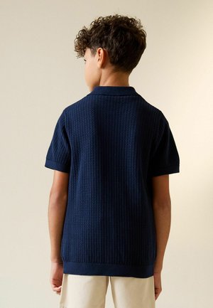 Marineblaues Polohemd mit kurzen Ärmeln, das ein strukturiertes Strickmuster und einen klassischen Kragen aufweist. Der Saum ist mit einem Rippabschluss versehen.