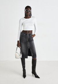 Gonna di jeans nera con zip frontale e spacco, crop top bianco a maniche lunghe, borsa argento e stivali neri con tacco a spillo fino al ginocchio, accessoriate con occhiali da sole bianchi.