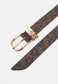 Bruine riem met een patroon, voorzien van een goudkleurige metalen gesp en logo. Heeft een gladde textuur en meerdere verstelgaten langs de band.
