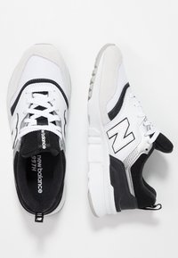 Białe i czarne buty sportowe wykonane z siateczki i zamszu. Posiadają sznurowadła, logo "N" oraz teksturowaną gumową podeszwę. Wyposażone w pętlę na pięcie.