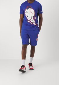 Modrá košile s krátkým rukávem s kreslenou postavičkou baseballového hráče, doplněná o odpovídající modré šortky. Výrazné červené akcenty a detaily loga.