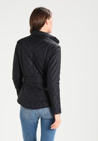 Casaco acolchoado preto com gola alta, cintura ajustada e mangas longas. Design minimalista sem hardware ou padrões visíveis.