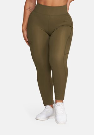 Zbliżenie na osobę noszącą oliwkowozielone legginsy z wysokim stanem, z bocznymi kieszeniami oraz białe sportowe buty.