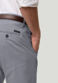 Grijze geruite broek met een textuurafwerking, voorzien van een achterzak met een knoop en een leren riem in bruin. Logo zichtbaar op de tailleband.