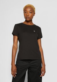 T-shirt nera in cotone con maniche corte e scollatura a girocollo. Presenta un piccolo logo bianco sul lato sinistro del petto e una vestibilità comoda.