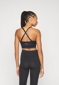 Svart sports-BH med kryssbak-remmer og logo, kombinert med høytlivs svarte leggings. Glatt, elastisk stoff med en tettsittende passform.