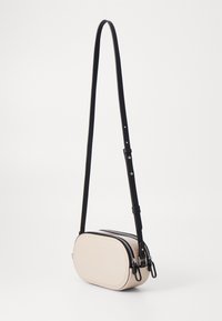 Borsa a tracolla in morbida pelle beige, forma ovale, con doppie chiusure lampo nere e tracolla nera regolabile. Texture liscia e design minimal.