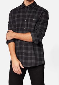 Zwart en grijs geruit overhemd met een kraag met knopen, voorzien van een sluiting met knopen aan de voorkant en lange mouwen die bij de manchetten zijn opgerold.