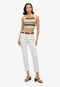 Gehaakte crop top met meerkleurige strepen, gecombineerd met witte, hoog in de taille zittende broeken. Een bruine gevlochten riem en sandalen met blokhakken maken de look compleet.