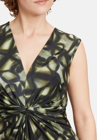 Ärmelloses Kleid in Dunkelgrün und Schwarz mit einem geometrischen Muster, das über einen V-Ausschnitt und ein verdrehtes Knotendetail an der Taille verfügt.