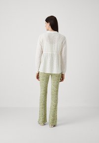 Hvit brodert bluse med lange ermer og peplumliv, kombinert med strukturerte grønne vide bukser med et flerfarget mønster.