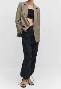 Blazer cruzado de patrón pata de gallo, combinado con un crop top negro ajustado y pantalones negros sueltos. Sandalias negras de tiras completan el conjunto.