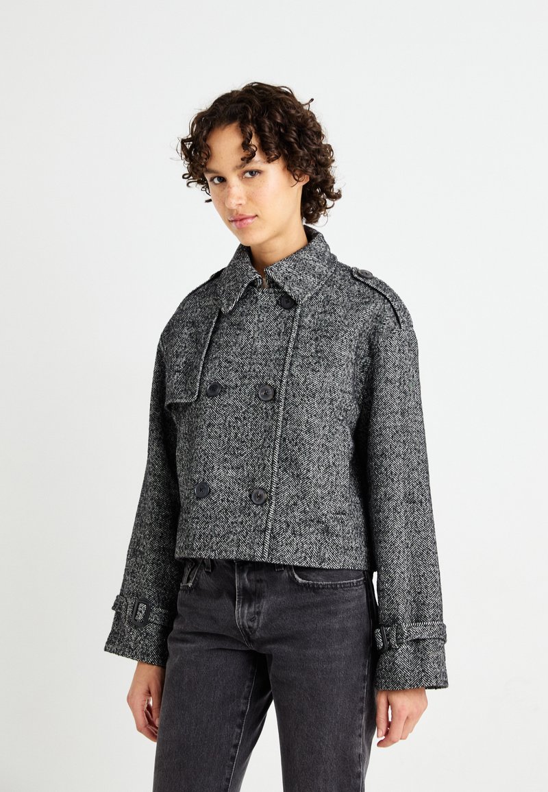 Grå herringbone peacoat, dobbeltknappet med store knapper, justerbare mansjetter og en strukturert krage. Kuttet lengde og teksturert stoff.