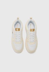 Baskets blanches et crème avec une tige en cuir lisse, un design à lacets, une boîte à orteils perforée et des accents de logo doré. Doublure en textile douce.
