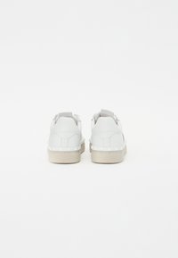 Baskets en cuir blanc au design bas, avec une semelle texturée et des détails de couture subtils, dotées d'une semelle en caoutchouc beige.