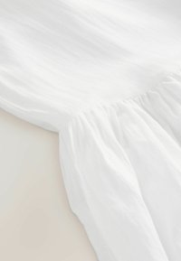 Tela blanca fruncida que muestra una textura suave y transparente con pliegues sutiles, que se transforma en una sección voluminosa en la parte inferior.