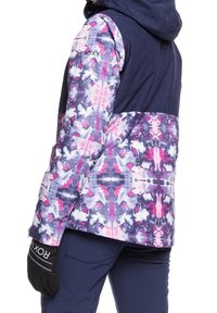 Schnee-Jacke mit einem oberen Abschnitt in Marineblau, gemustertem unteren Abschnitt in Rosa, Lila und Weiß. Verfügt über eine Kapuze und schwarze Handschuhe mit Branding.