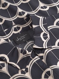 Blusa blu navy con motivo geometrico crema, presenta un colletto, dettagli con zip e un'etichetta che legge "Vaschio Stockholm S." Texture del tessuto liscia.