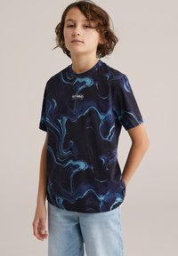 Tricou negru cu model marmorat în nuanțe de albastru și teal, mâneci scurte, decolteu rotund și un logo în centru. Asortat cu blugi bleu deschis.