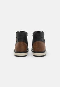 Botas de cuero negras y marrones hasta el tobillo con un acabado texturizado, que cuentan con dobles cremalleras y una suela blanca contrastante. Acolchado suave visible en la parte superior.