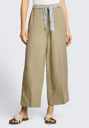 Beige, weit geschnittene, verkürzte Hose mit einem blau-weiß gemusterten Stoffgürtel, der an der Taille gebunden ist, getragen mit beigen Slides.