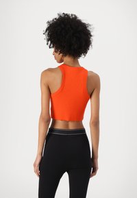 Haut court orange à côtes avec un col montant et sans manches, associé à des leggings noirs taille haute avec une ceinture contrastante.